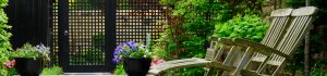 Fencing & Gates - Garden trellis fence with trellis gate, bowl planters with flowers in bloom, two wooden garden deckchairs in the foreground