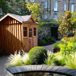 Garden Structure - Wooden shed in background with stone-built seating area backed by plants in foreground